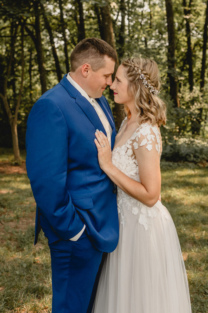 Close up of young newlyweds in royal blue suit and boho dress with foreheads together