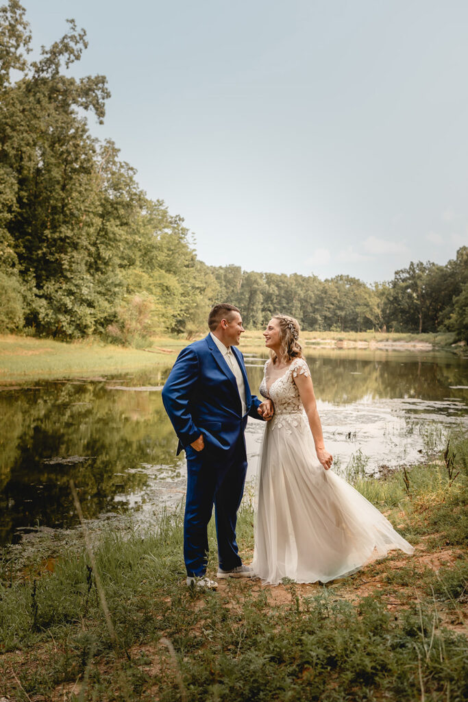 Newlyweds smile towards the other as bride sways dress in front a small lake at Quail Ridge Park