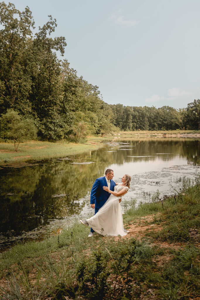 Newlyweds dip before a kiss in front a small lake at Quail Ridge Park