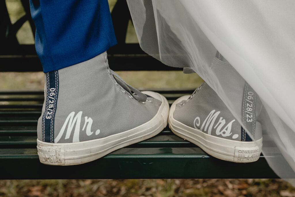 close up of grooms right shoe next to the bride's right showing their wedding details on custom match gray hightop Converse