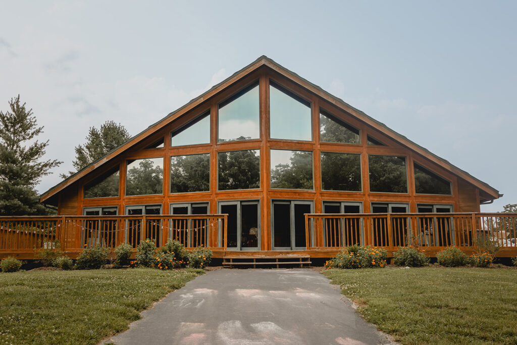 Exterior shot of Quail Ridge Lodge, a wide A-frame style wood venue with a wall of windows above sliding glass doors