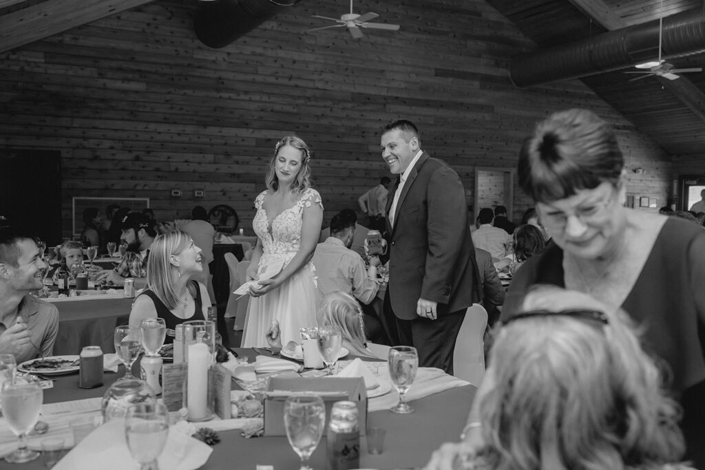black and white shot of bride and groom candidly greeting a table of guests during dinner