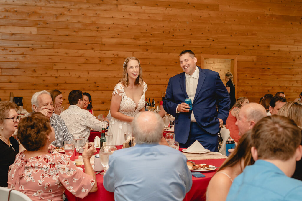 wide shot of bride and groom candidly laughing as they greet a table of guests during dinner