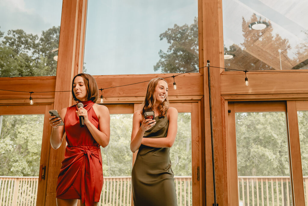 bride's sisters give joint wedding toast in front of wall of windows to outside greenery