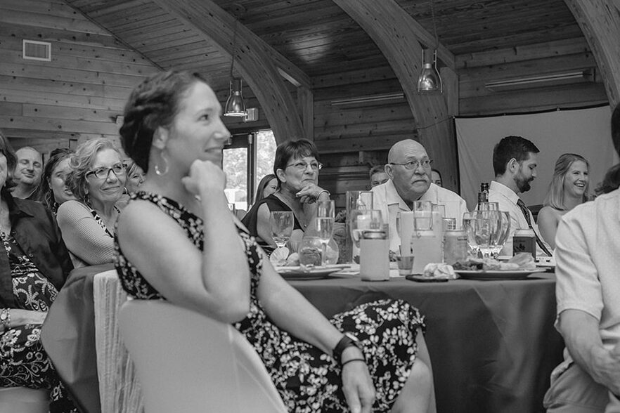 Candid black and white shot of groom's parents listening to wedding toasts