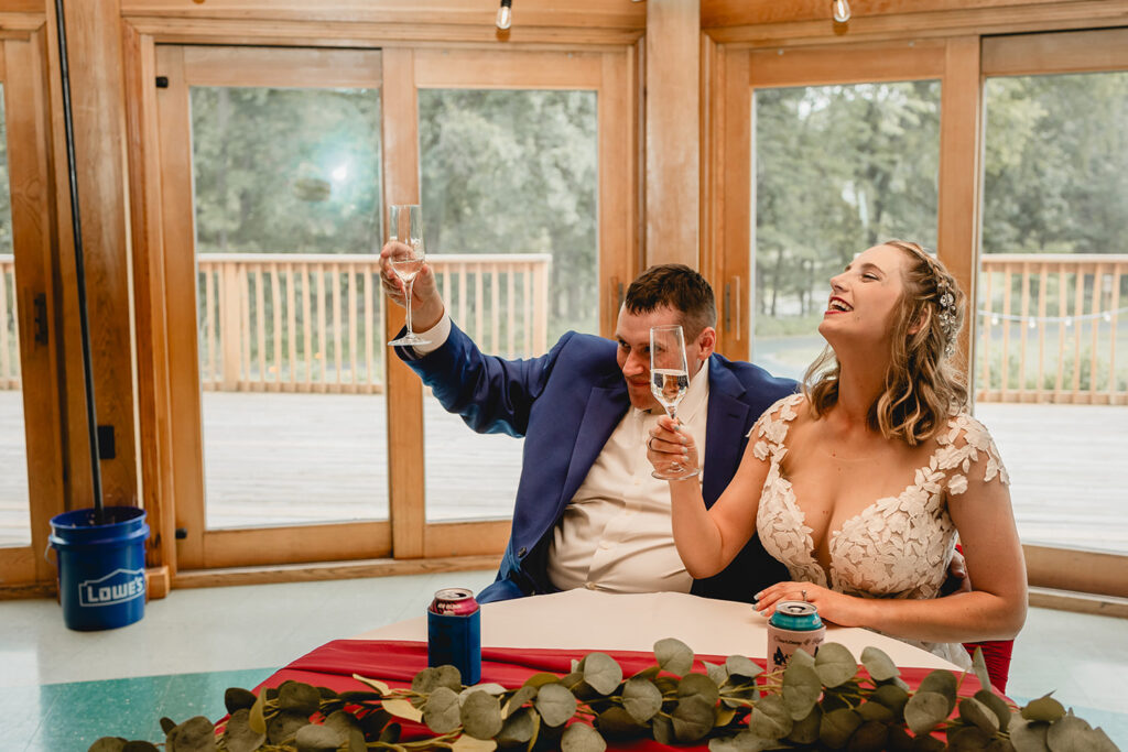 Groom in royal blue suit and bride in boho dress happily raise their glasses to a toast