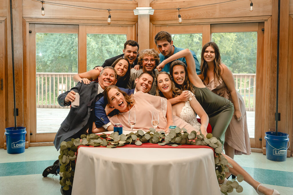 bride and groom seated at their sweetheart table while a group of guests lean in close to give noogies and lay across their laps 