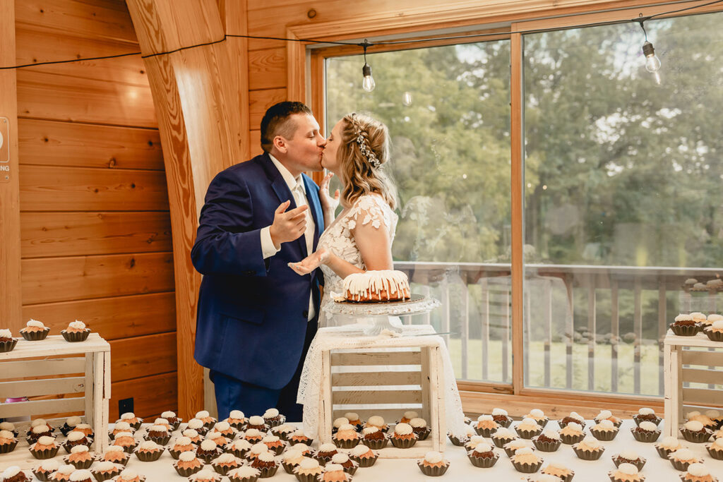 newlyweds kiss behind dessert table full of cupcakes with hands outstretched covered in icing