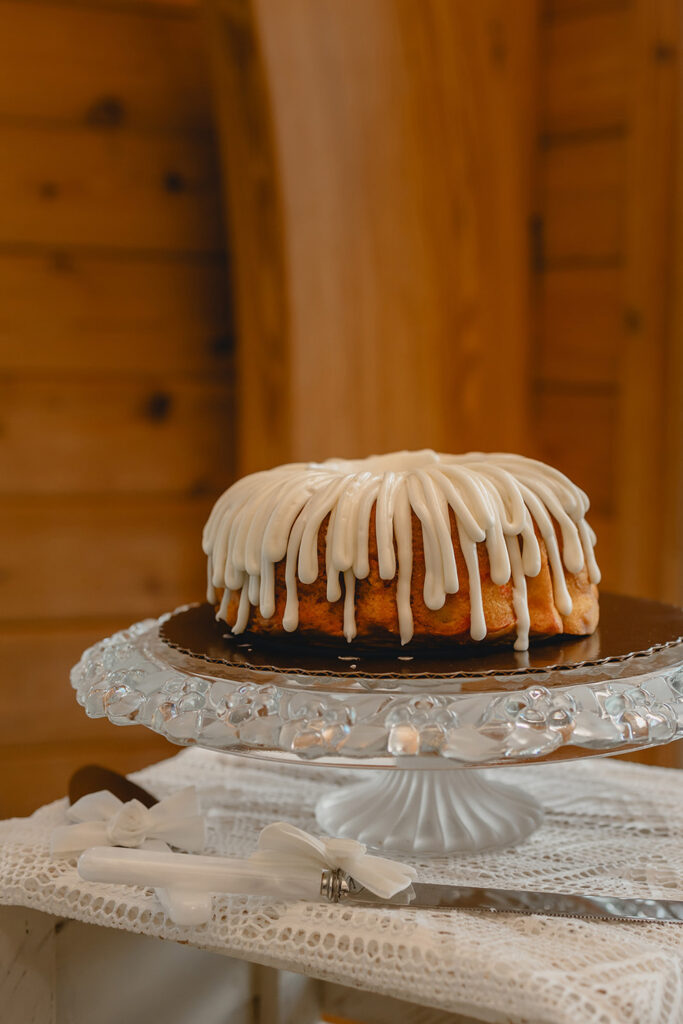 close up of small vanilla bundt cake with white icing on glass cake stand