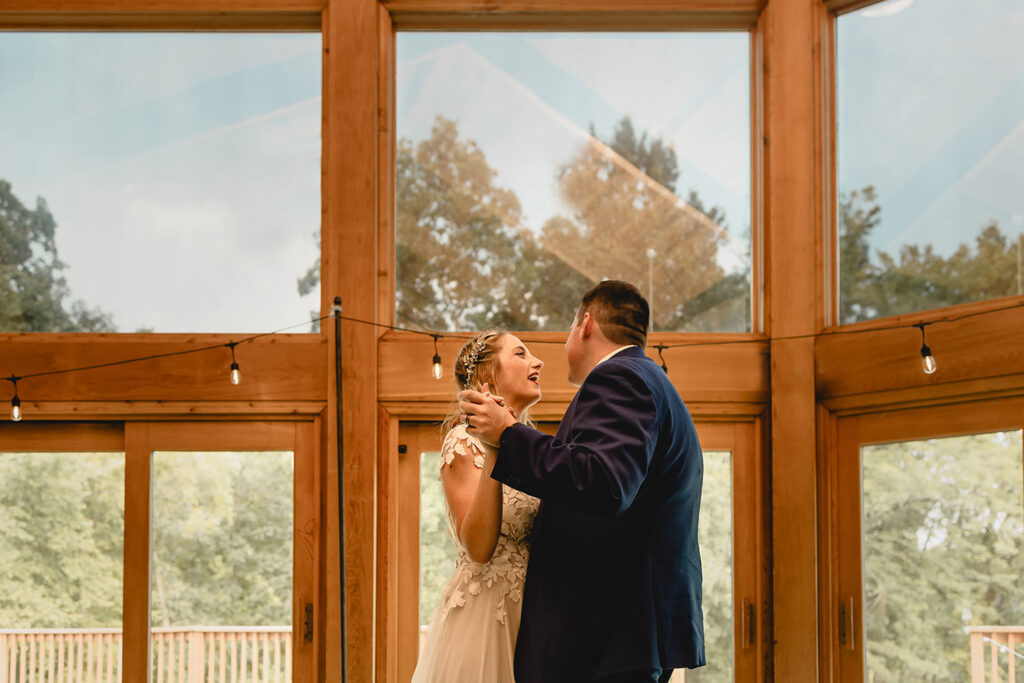bride and groom share a first dance in front of window wall in Quail Ridge Lodge