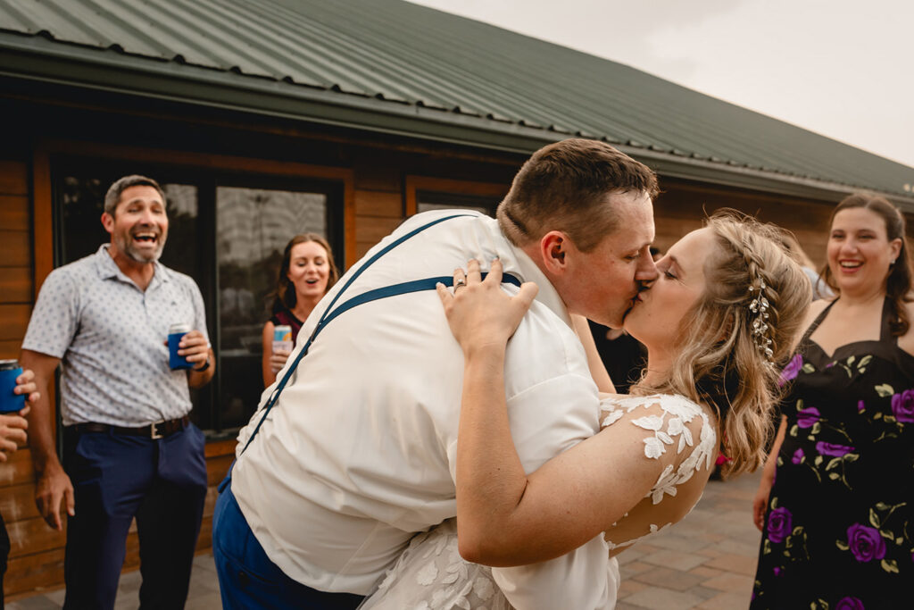groom surprises his bride with a kiss in front of a circle of guests