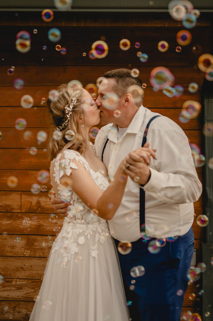 Close up of bride and groom kissing behind a sea of bubbles in front of a wooden wall