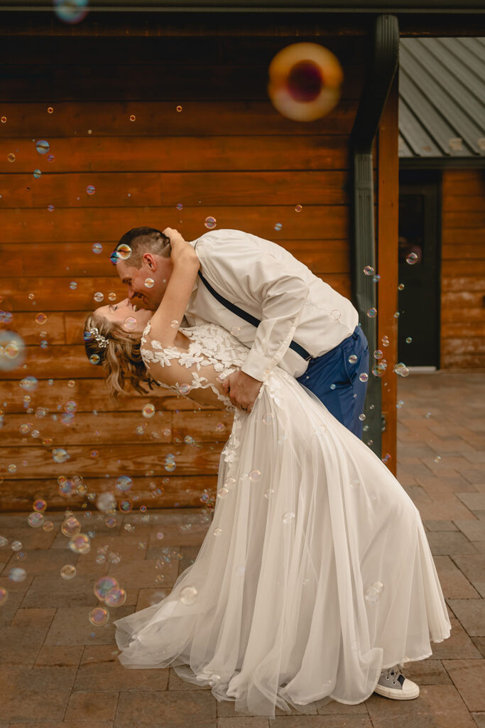 Full body shot of bride and groom dipping back into laughter surrounded by bubbles
