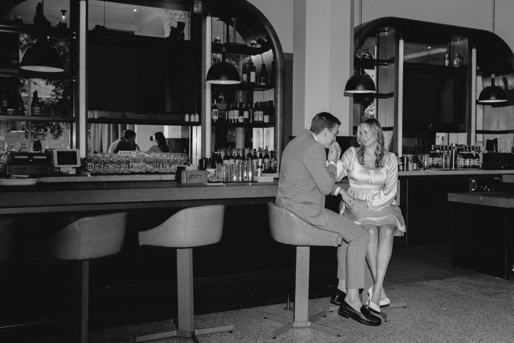 wide shot of the bar a young man kissing the hand of girlfriend on bar stools along the lounge bar at the Last Hotel STL