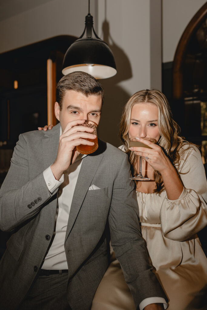 moody shot of young couple taking sips of their cocktails as they look to camera