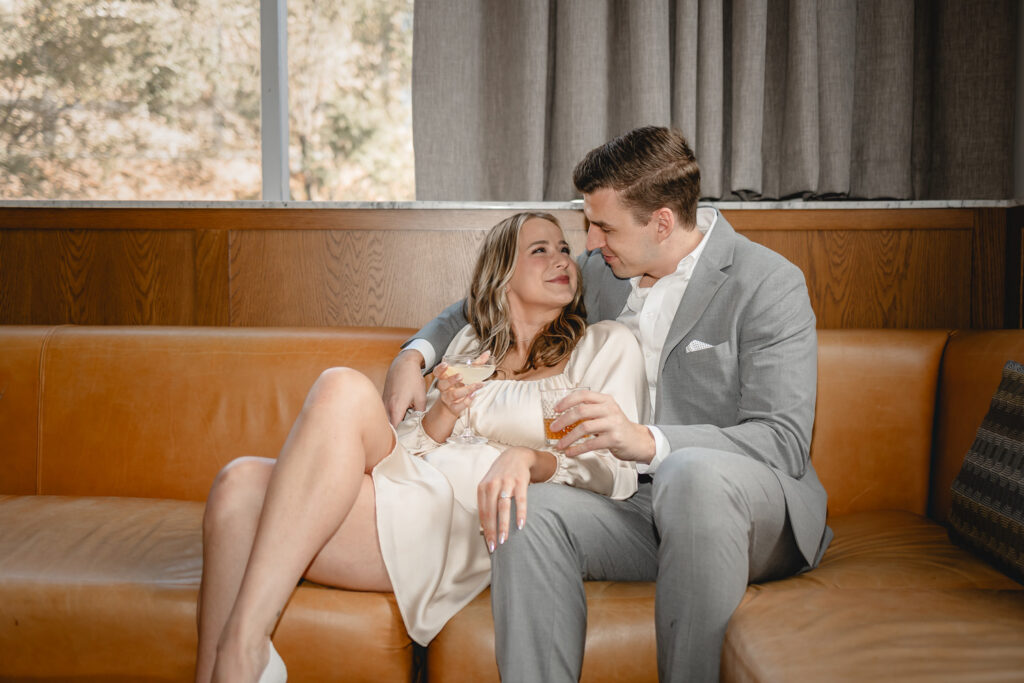 young stylish dressy couple relax and cuddle up with cocktails on a long leather couch