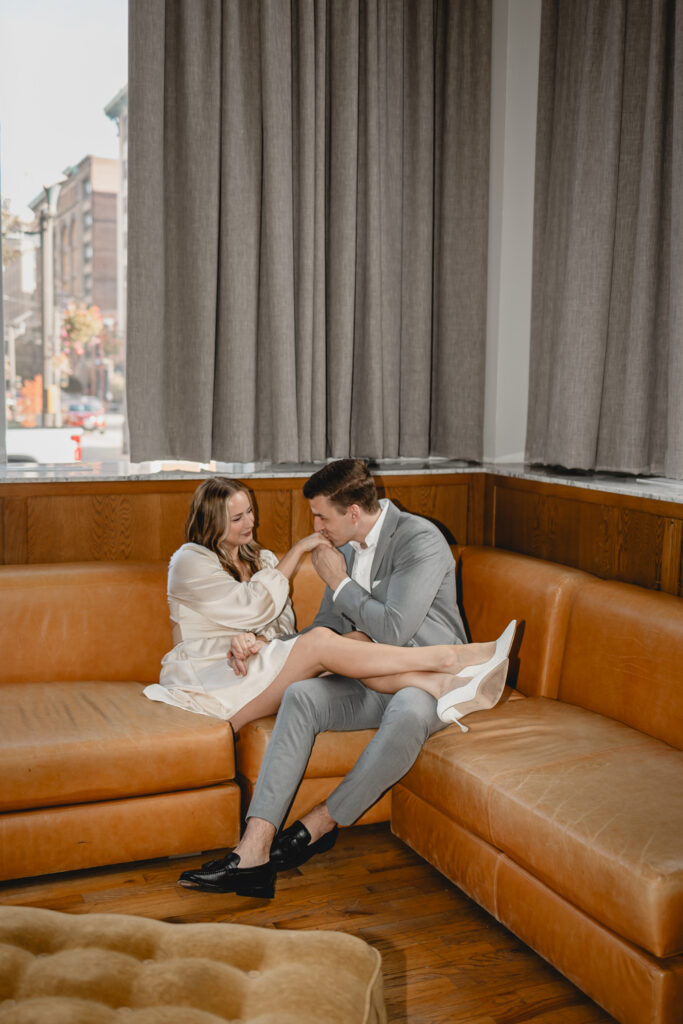 far shot of a man romantically kissing his girlfriends hand in the corner of a retro orange couch