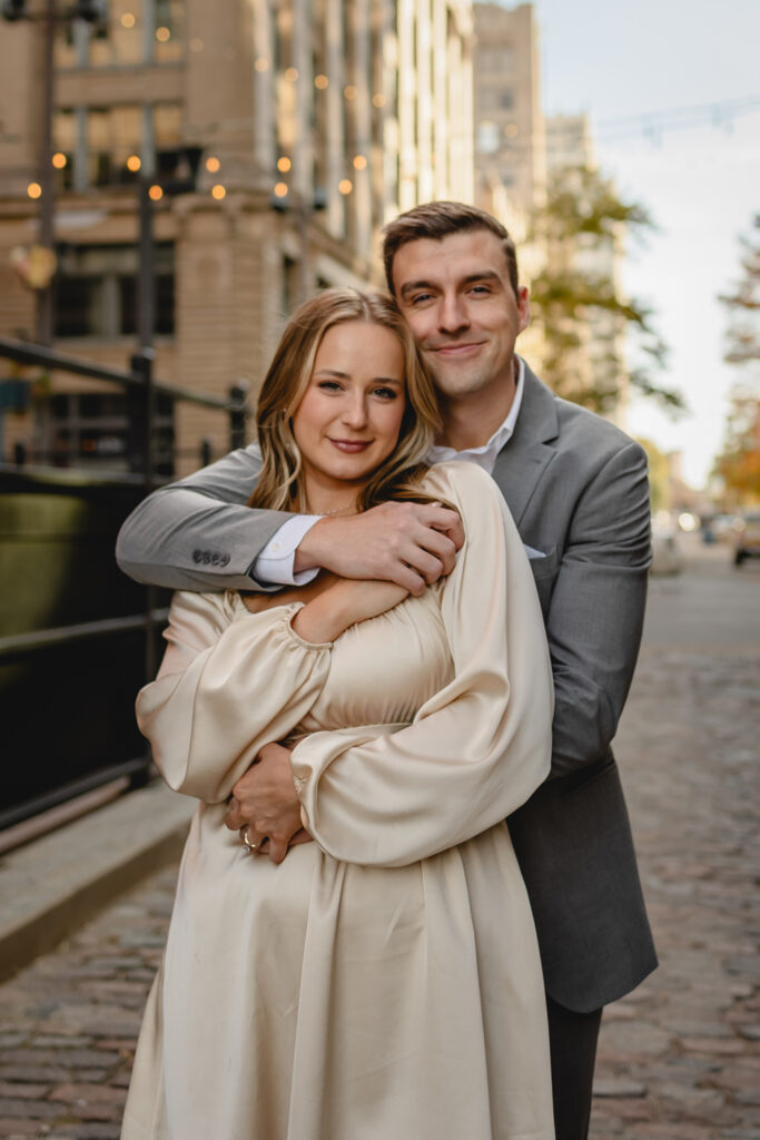 close up portrait of a stylish dressy couple holding hands and wrapped in a hug smiling toward the camers