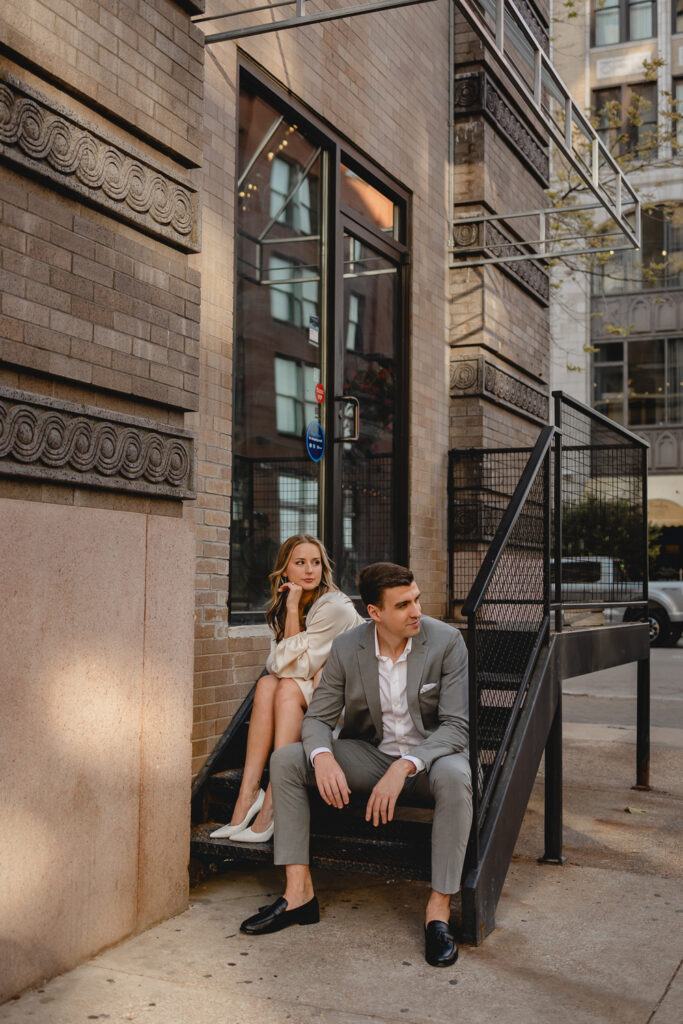 young couple seated on downtown iron stoop steps and look off camera