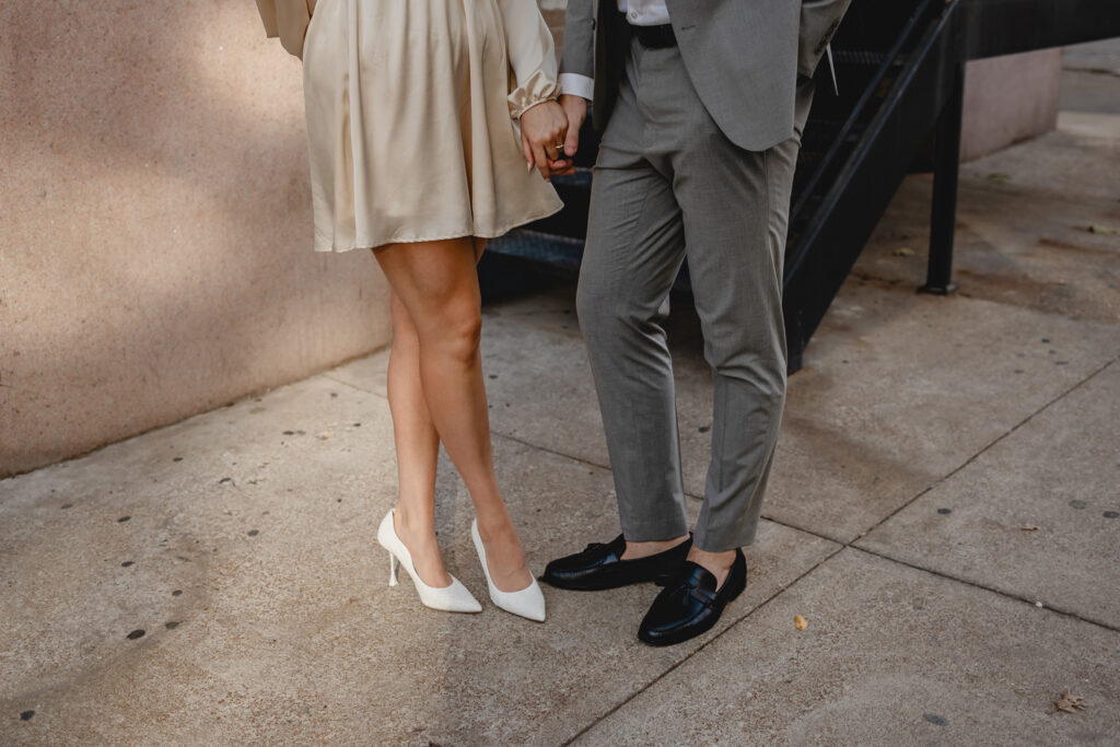 waist down shot of couple holding hands to feature their high heels and chic black loafers