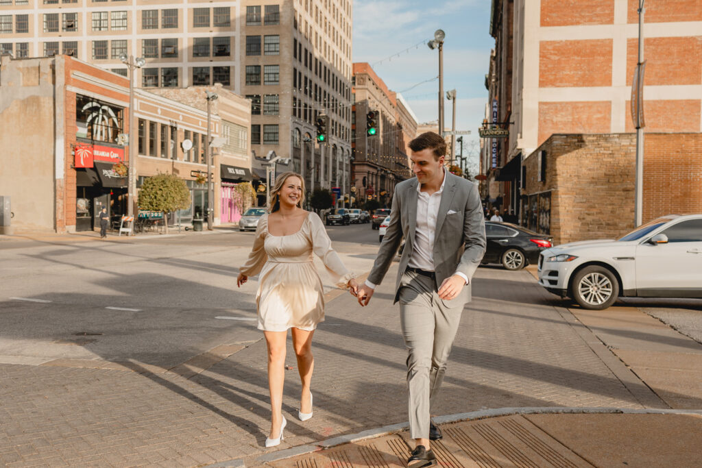 candid shot of couple holding hands and walking across a downtown intersection