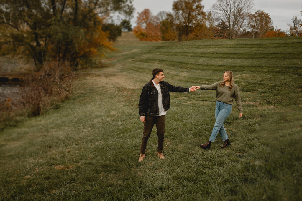 couple walking down a grassy hill arms extending toward the other to hold hands