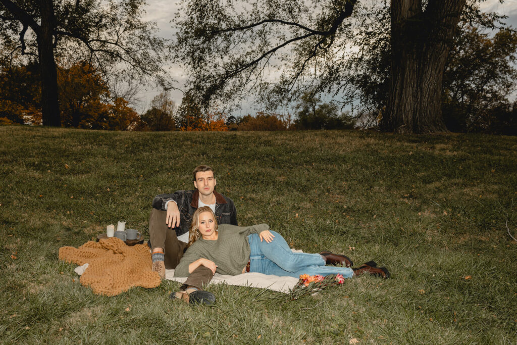 direct flash shot of a women laying on her side over her boyfriend's extended leg as he sits up behind her on a grassy hill