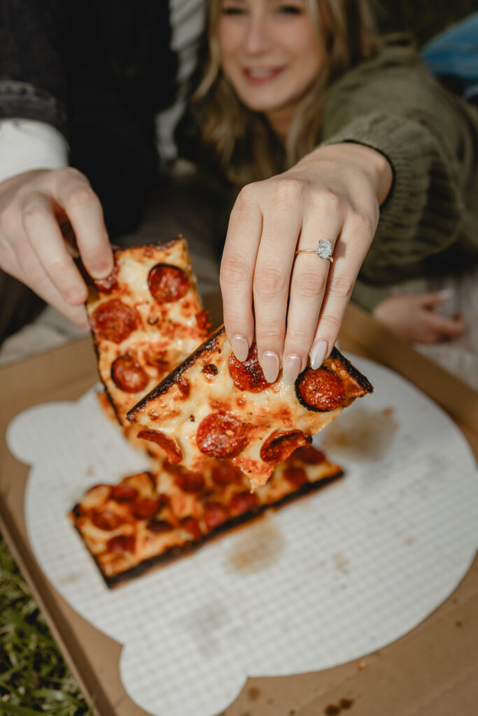 close up of couple holding pizza slices to camera to bring focus to a diamond engagement ring