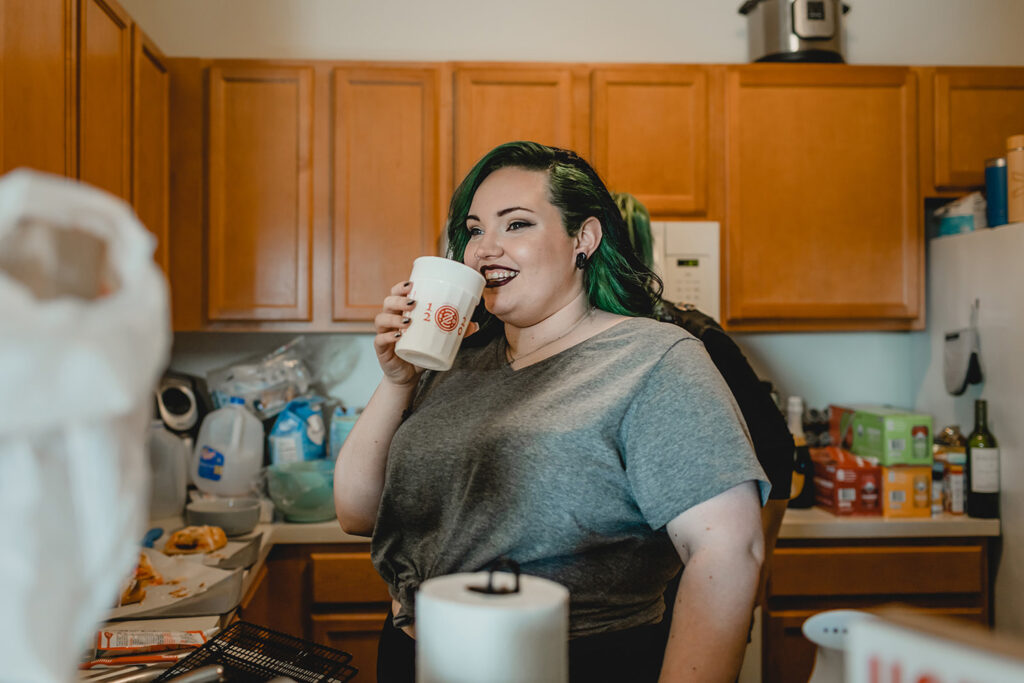 young bride smiles across the counter in her kitchen towards her friends as she sips hot cocoa