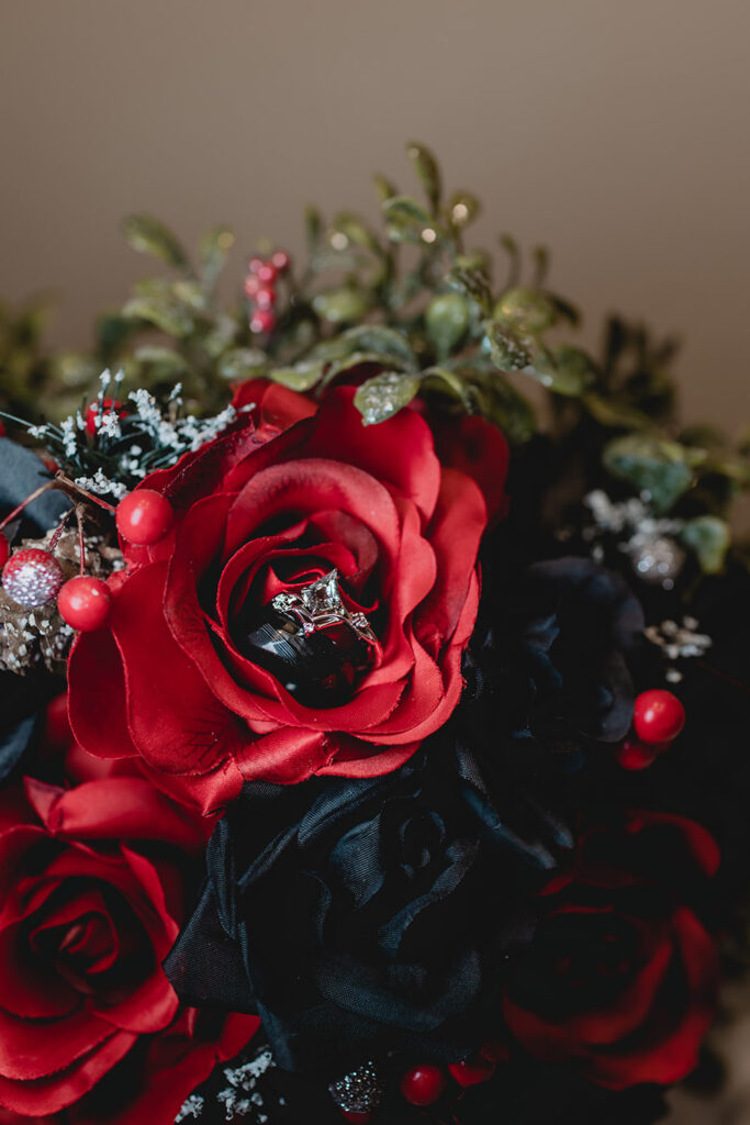 a gothic-style wedding ring sits inside a bouquet of red and black roses