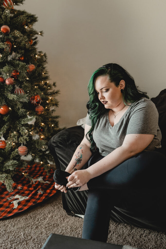 bride seated on her couch putting on her shoes beside her black, white and red-decorated christmas tree