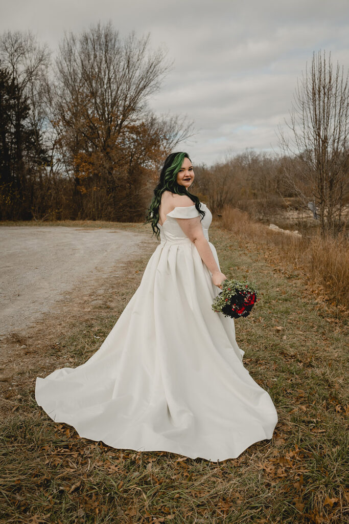 young bride with black and green hair looks back over the shoulder towards the camera with her black and red bouquet