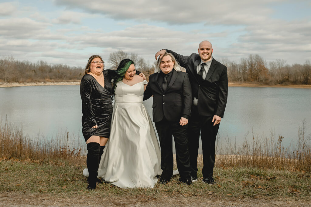 candid group shot of the maid of honor, bride, groom and best man laughing and interacting with each other in front of a winter lake