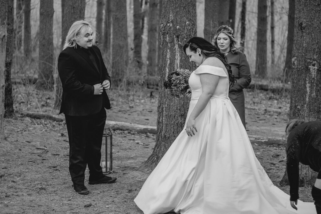 grooms smiles at his bride as she fluffs her dress to settle in for their wedding ceremony in a longleaf pine forest