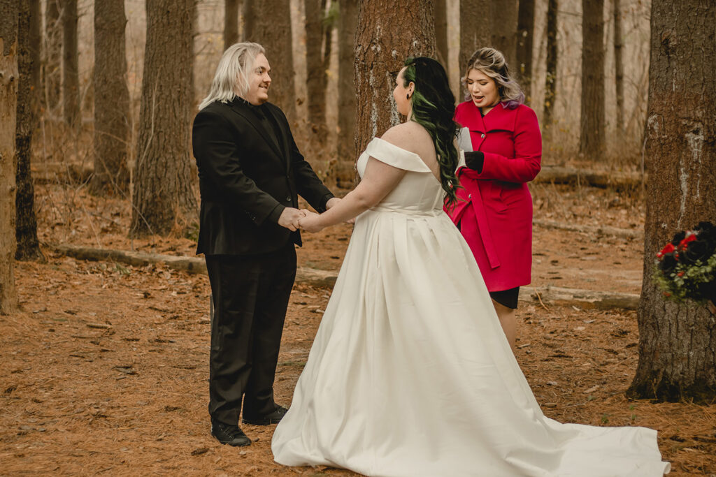 bride and groom holding hands during their outdoor winter ceremony in front of officiant in bright red coat
