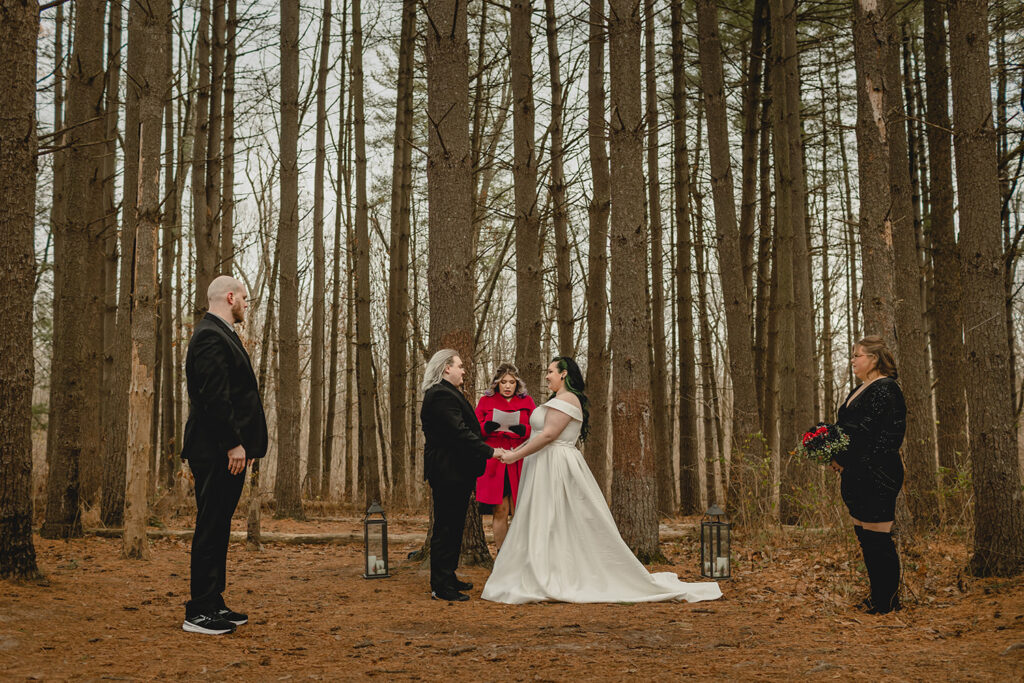 young bride, groom and officiant centered between the best man and maid of honor in a grove of tall pine tree trunks