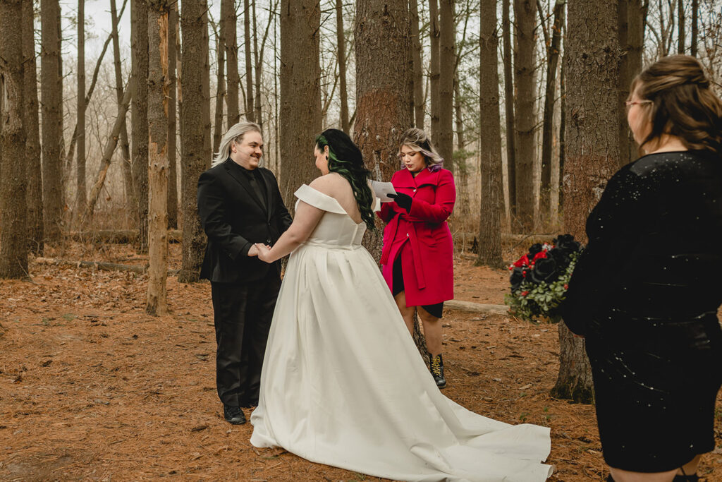 bride and groom holding hands during their outdoor winter ceremony in front of officiant in bright red coat