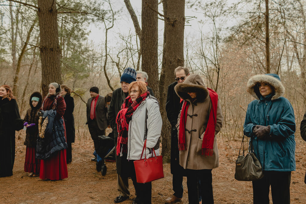 small group of people in heavy winter clothing looking off frame toward the ceremony