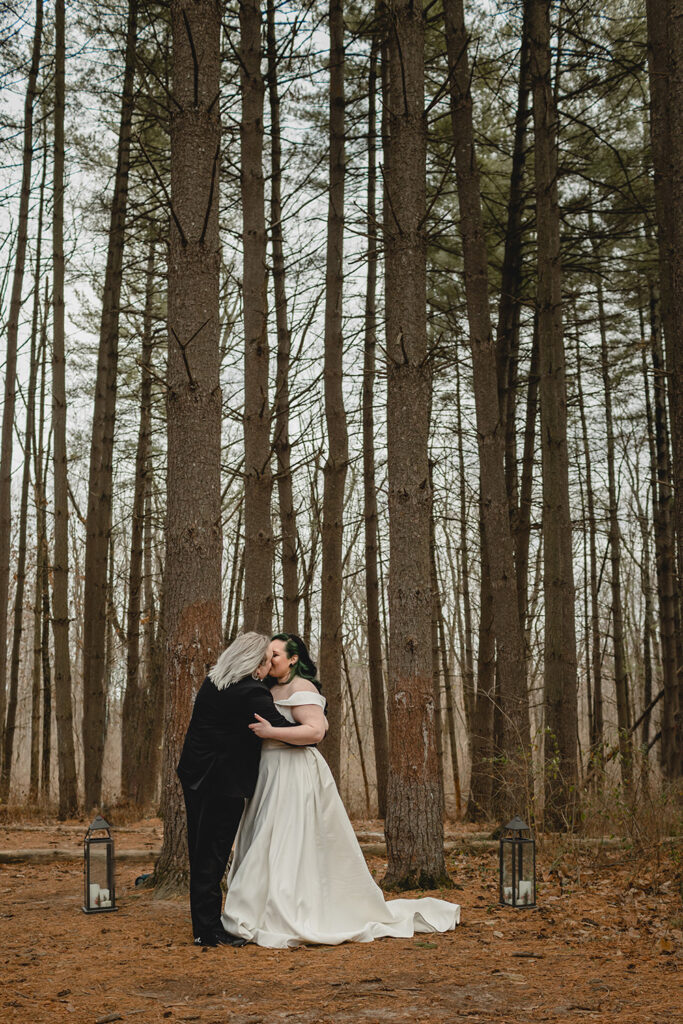 far shot of bride and groom's first kiss in the pine grove