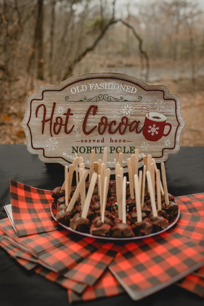 plate of chocolate covered cocoa bombs on popsicle sticks sit in fron of a wooden hot cocoa sign