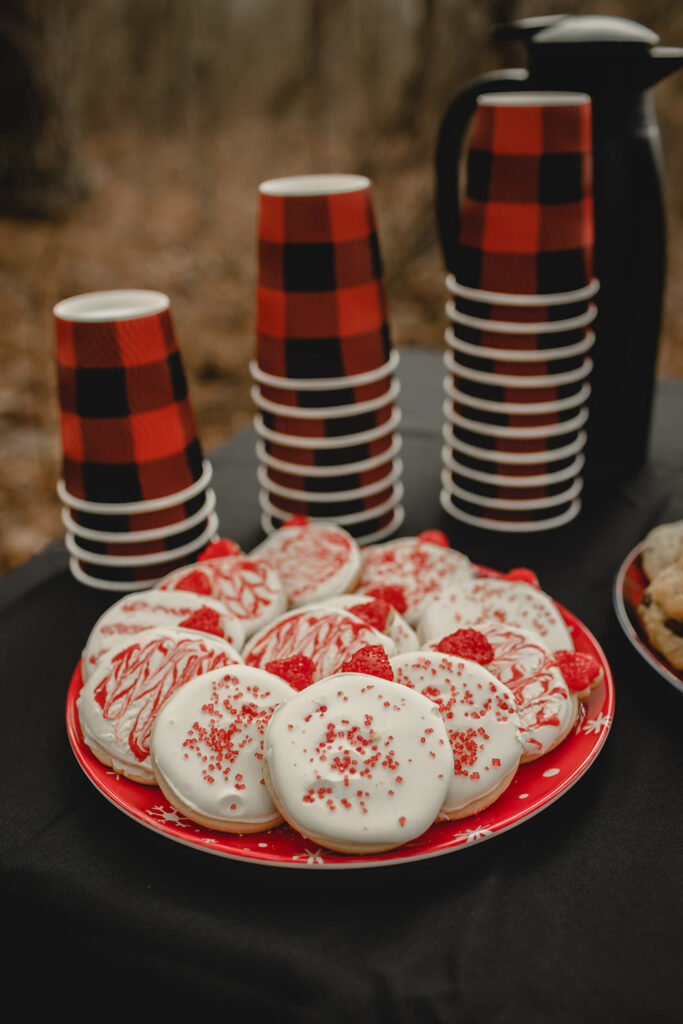 three stacks of plaid black and red cups behind a plate of homemade white and red iced sugar cookies