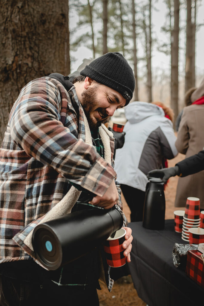 Man in plaid coat pouring a black canister of hot chocolate into a cup
