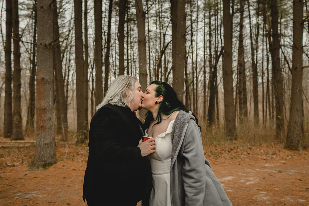 bride and groom kissing in a forest while holding cups of hot chocolate