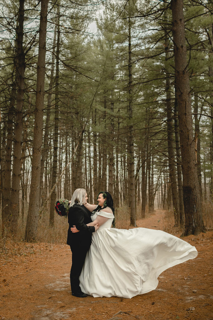 bride and groom embracing in a beautiful pine forest as the bride' dress tosses in the wind