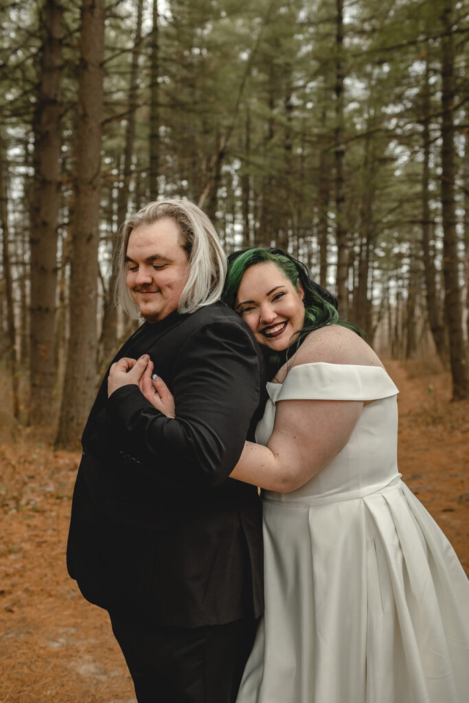 young smiling bride with black and green hair hugs her new husband from behind