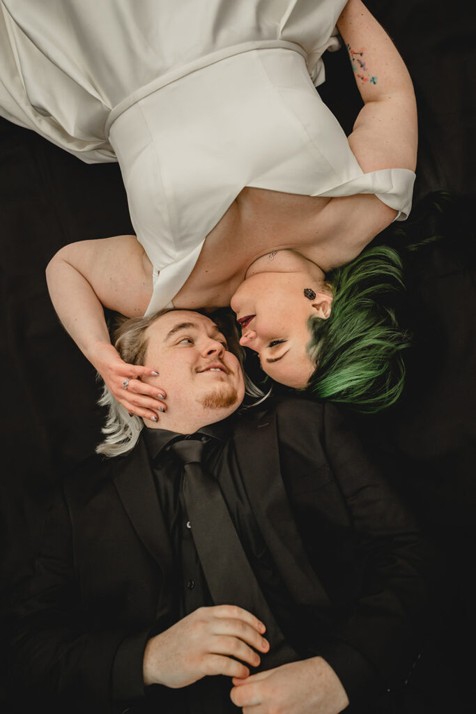aerial shot of bride and groom laying on a black sheet with heads together and bodies in opposite directions