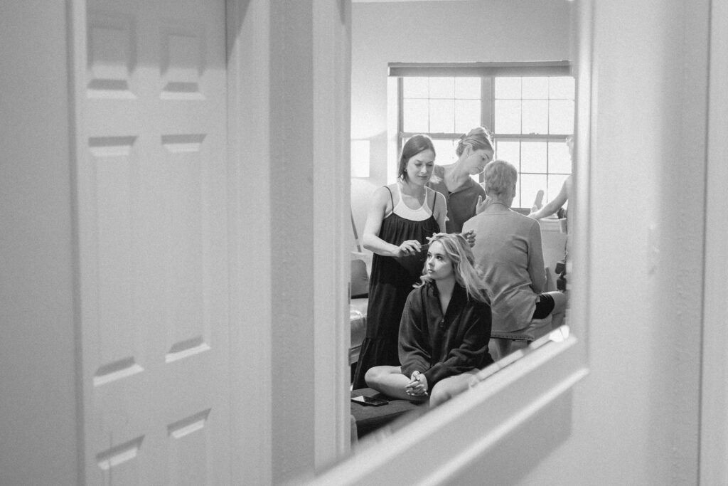 Black and white photo of bridesmaid getting her hair curled in a mirror