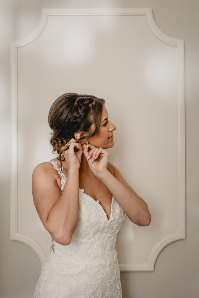 Bride with braided hair putting in earrings in her wedding dress