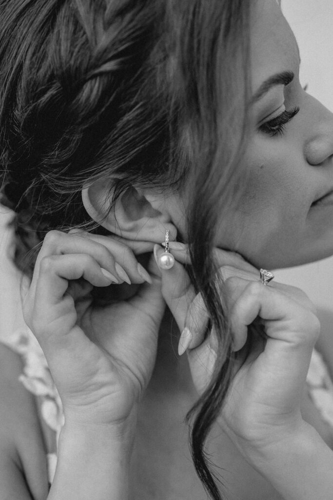 Close up photo of bride putting in pearl earings