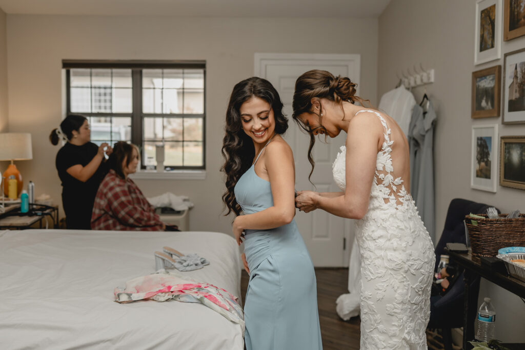 Bride helping a bridesmaid zip up her dress before wedding